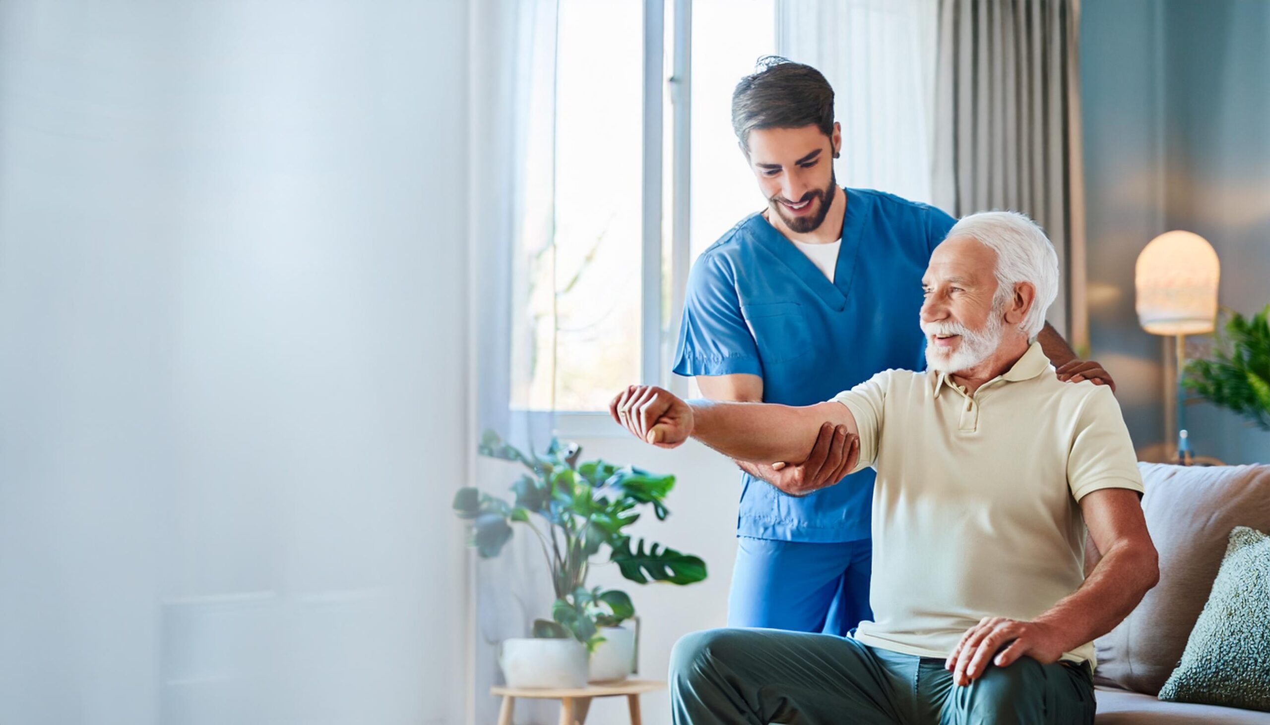 Un fisioterapeuta profesional, vestido con uniforme azul, asiste con una sonrisa a un hombre mayor durante una sesión de rehabilitación en casa. El ambiente es luminoso, acogedor y tranquilo, con plantas decorativas y mobiliario moderno que complementan el entorno